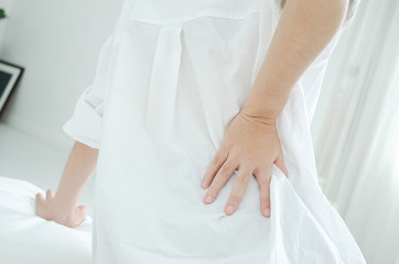 Women wear white shirts and pink pants on the bed in a room with hip pain in the morning.Asian women Have back pain In the morning.Back pain is caused by a mattress.Do not focus on objects.