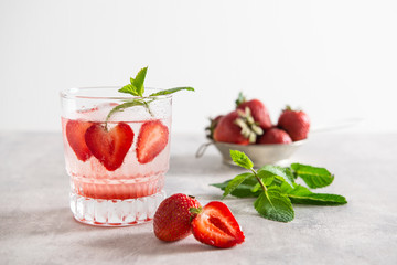 Fresh lemonade with ice, mint and strawberry in glass on white table background. Cold refreshing summer drink. Sparkling glasses with berry cocktail. Copy space