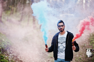 Obraz premium Street style arab man in eyeglasses hold hand flare with red and blue smoke grenade bomb.