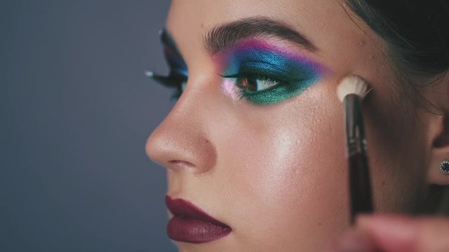 Professional make-up artist makes make-up to a beautiful girl model, feathering powder, highlighter, foundation cream with a special brush for makeup