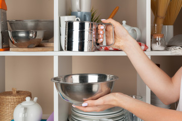 Woman hand taking dishware pieces from shelf in kitchen