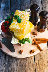 Variety of cheeses on the old, rustic table.Spices, cheese, tomatoes and lemon with lime on the cutting Board.In the sunlight.