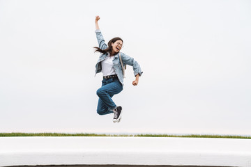 Image of cheerful teenage girl having fun and rejoicing while walking along white wall outdoors