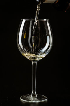 White wine being poured in a wine glass on a dark background