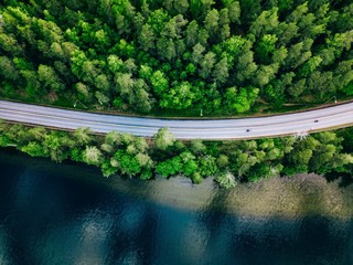Aerial view of road between green forest and blue lake in Finland