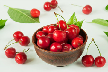 Close-up of ripe red sweet cherry with branches and leaves in a ceramic brown bowl on a white background. Selective focus.