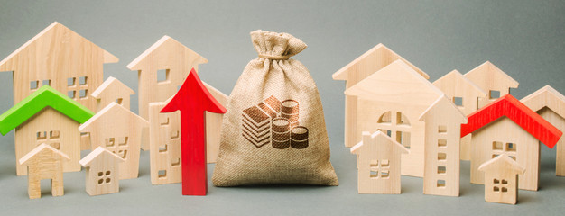Red arrow up, money bag and miniature wooden houses. The concept of rising property prices. High...