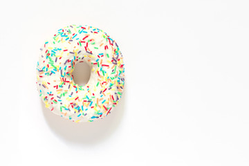 White frosted donut with colorful sprinkles  on white background.