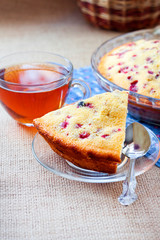 Piece of cowberry pie on glass plate and cup of tea