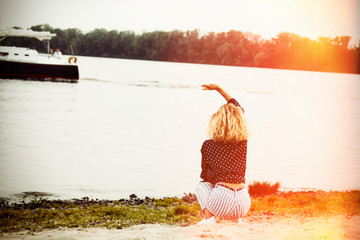 cute stylish curly girl model sits and dreams on the river bank in summer