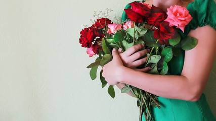 hands of a girl in a green dress holding flowers of roses.