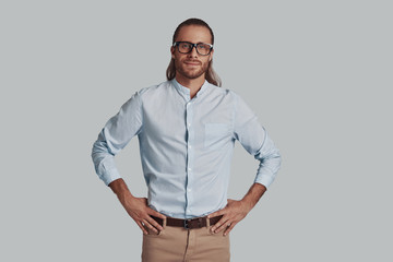 Fototapeta premium Positively charming. Handsome young man looking at camera and smiling while standing against grey background
