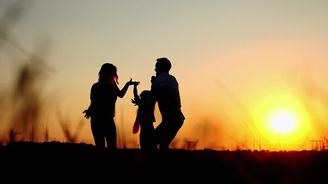 Silhouettes of happy parents throw up their daughter and hugs at summer sunset in the field, enjoying their vacation