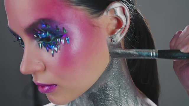 Professional makeup artist at work. Beauty industry of cosmetics backstage of professional makeup. Makeup artist covers model's neck and chest with metallic makeup