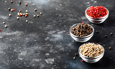Pepper set. Black, white and pink rose peppers in bowls, assorted spices on gray kitchen table, selective focus