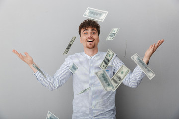 Portrait of young caucasian man dressed in shirt smiling on camera while standing under falling...