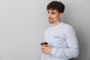 Portrait of brunette young man dressed in shirt smiling and posing on camera with takeaway coffee...
