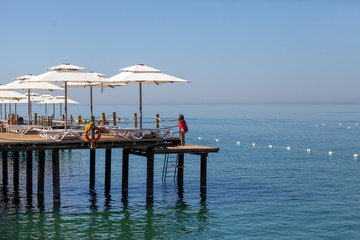 Parasols and sunbeds stand one after another on the touristic wooden pier with an infinity sea view.