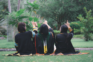 Fototapeta na wymiar Thai group women wearing graduation dresses sitting in in the park from the back.