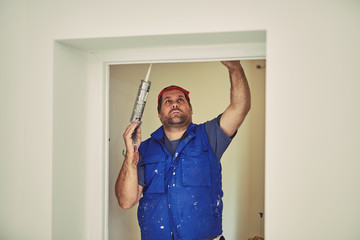 Worker using silicone for walls and door frame inside the house - renovation fixes.