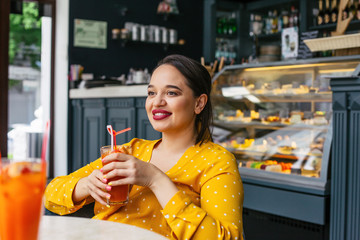 Happy beautiful plus size woman smiling and drinking healthy smoothie in cafe