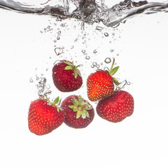 Close-up photo, on a very short exposure, strawberries falling into the water on a white background close up