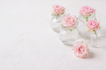 Obraz na płótnie Canvas Small pink roses in glass vases on a wooden background.