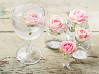 Small  pink roses in glass vases on a wooden background.