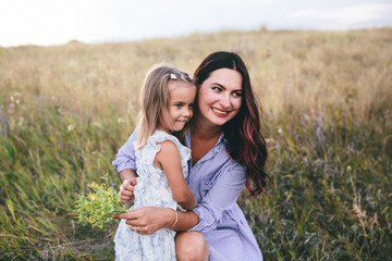 Mother and daughter are relaxing and smiling in wheat field at spring time.