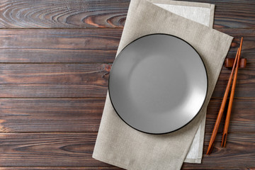 Empty grey round plate with chopsticks for sushi on wooden background. Top view with copy space