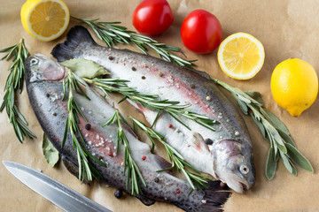 Two raw fish. Fresh trout with lemons, tomatoes and greens on the table.