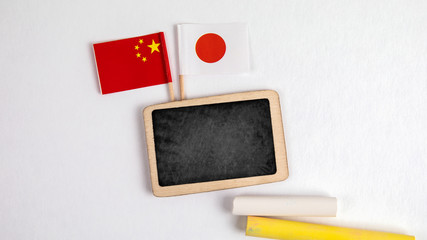 Japan and Chinese flags. Small whiteboard with chalk. Top view on a white background. Mockup, copy space.