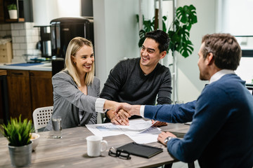 Young happy couple handshaking with financial advisor at their home.