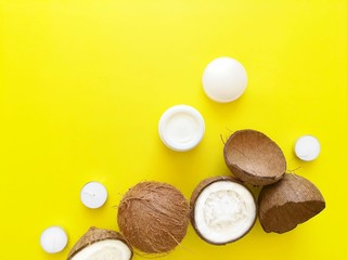 Coconuts, face cream or body oil on a bright yellow background. Skin care concept, natural organic cosmetics, summer shopping. Top view, flat lay, copy space for text.