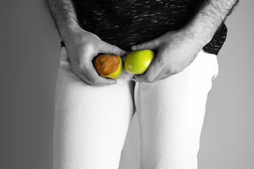 A man at the level of the genitals , holding a ripe and rotten apple. Disease for men. The concept of protection of sexually transmitted infections. Testicular cancer. Close up