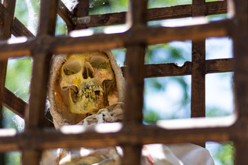 Scary old human skeleton in a wooden cage in torn clothes and blurred sky background. A medieval...