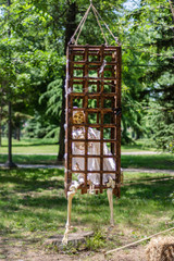 Old human skeleton in a wooden cage hanging on a tree and green spring forest in the background. A...