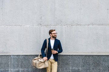 Portrait of attractive businessman wearing eyeglasses holding paper cup and carrying bag