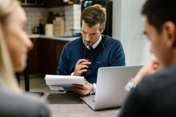 Pensive financial advisor reading reports while having a meeting with a couple.