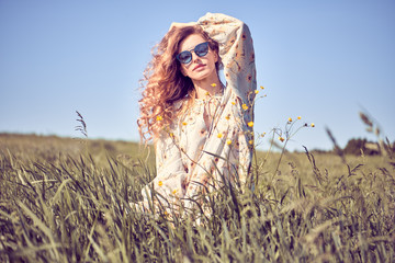 Fashion portrait. Young Beautiful redhead woman walking at grass field, enjoy nature. Joyful Model girl in summer sunlight, fashionable stylish dress. Outdoor, authentic sunny nature concept