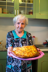 Elderly woman in the kitchen with a pie in his hands.