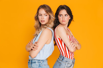 Portrait of two offended blonde and brunette women 20s in summer wear frowning while standing back...