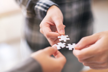 Closeup image of many people hands holding and putting a piece of white jigsaw puzzle together