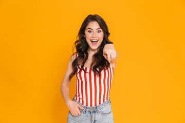 Portrait of happy young woman in striped t-shirt looking at camera and pointing finger at camera with her hand in pocket
