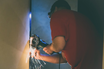 A man repairs a door in the basement of his house using a manual grinding machine.