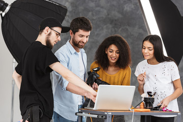 Portrait of working multiethnic people looking at laptop while photo shooting with professional...