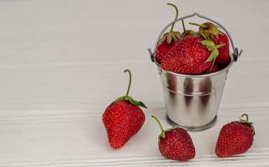 Fresh summer ripe strawberries in a small bucket on a white wooden background