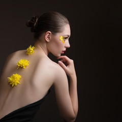 Young woman spa. Yellow flowers along her back, face and body in the shade. Back view. Dark background