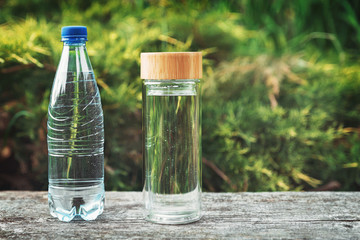 Plastic water bottle and reusable stylish glass bottle on the background of green plants with space for text.Opting for reusable utensils.Zero waste concept.Green and conscious lifestyle concept.