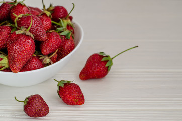 Fresh summer ripe strawberries in a white plate on a white wooden background